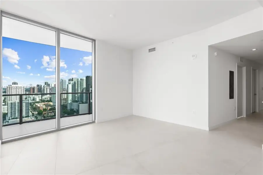 Floor-to-ceiling windows, private balcony with metal railing, large-format tile flooring, recessed lighting, and expansive city skyline scenery