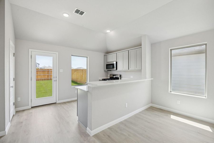 Kitchen with light wood-style floors, light countertops, stainless steel appliances, a peninsula, and lofted ceiling