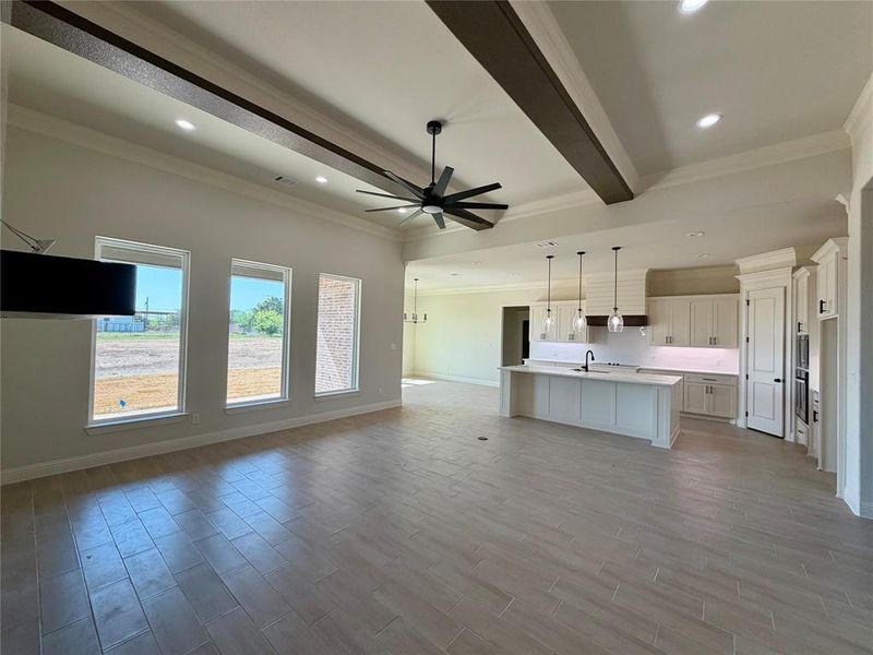 Kitchen featuring open floor plan, crown molding, beam ceiling, an island with sink, and light wood-style flooring Kitchen featuring open floor plan, crown molding, beam ceiling, an island with sink, and light wood-style flooring