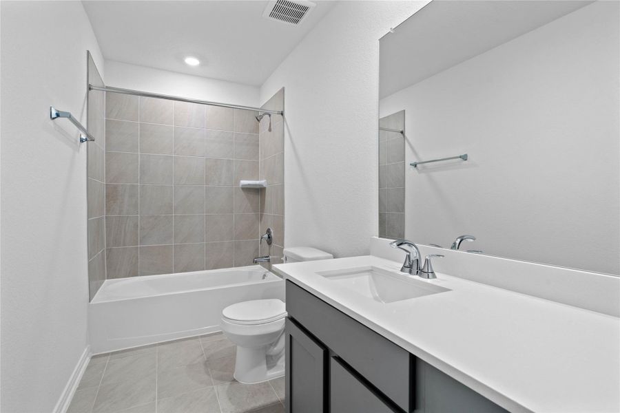 The secondary bathroom showcases tile flooring, a bath/shower combo with tile surround, a vanity with knee space and stunning light countertop, a mirror, sleek fixtures, and contemporary finishes throughout.