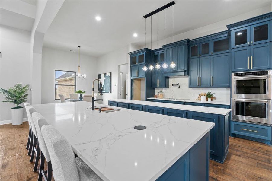 Kitchen featuring stainless steel double oven, blue cabinets, and a center island with sink