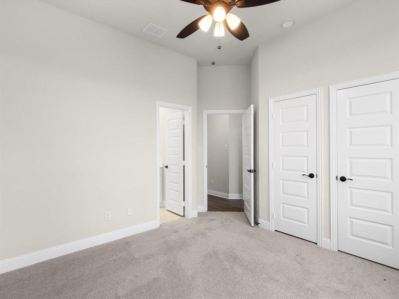 Unfurnished bedroom with light carpet, a ceiling fan, and a high ceiling