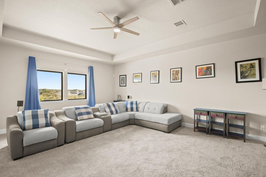 Carpeted living room featuring a raised ceiling and ceiling fan Carpeted living room featuring a raised ceiling and ceiling fan