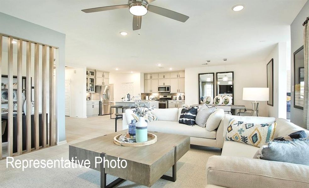 Open-concept living area with recessed lighting and a ceiling fan, featuring a light wood-finish room divider and a kitchen with light cabinetry and stainless steel appliances