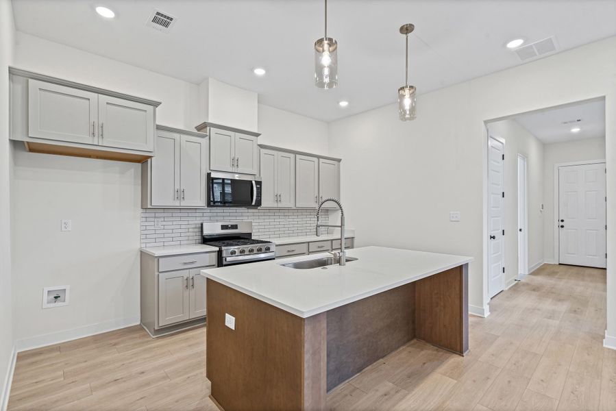 Kitchen featuring light gray cabinetry, white subway tile backsplash, stainless steel appliances, and an island with a white countertop and integrated sink Kitchen featuring light gray cabinetry, white subway tile backsplash, stainless steel appliances, and an island with a white countertop and integrated sink
