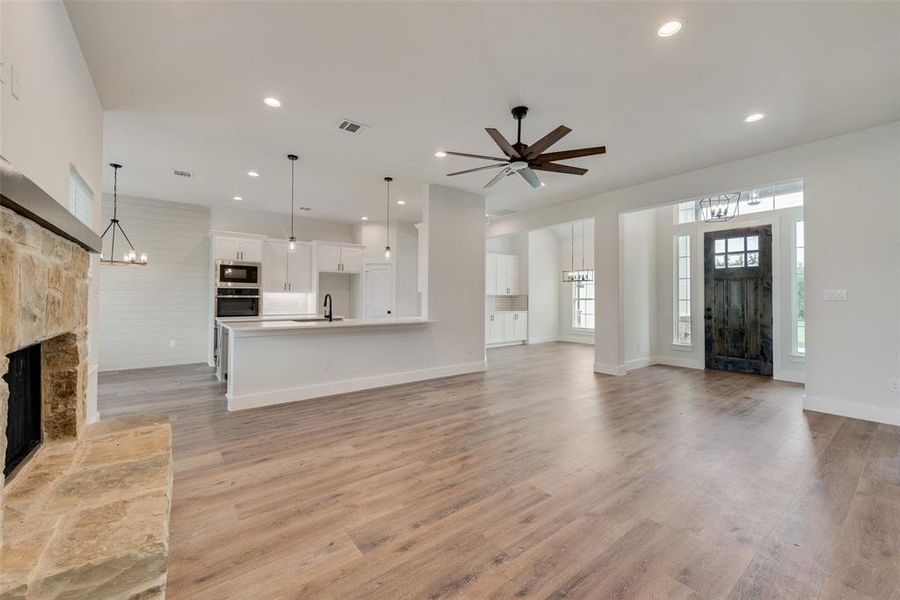 Unfurnished living room featuring sink, light hardwood / wood-style flooring, ceiling fan with notable chandelier, and a stone fireplace