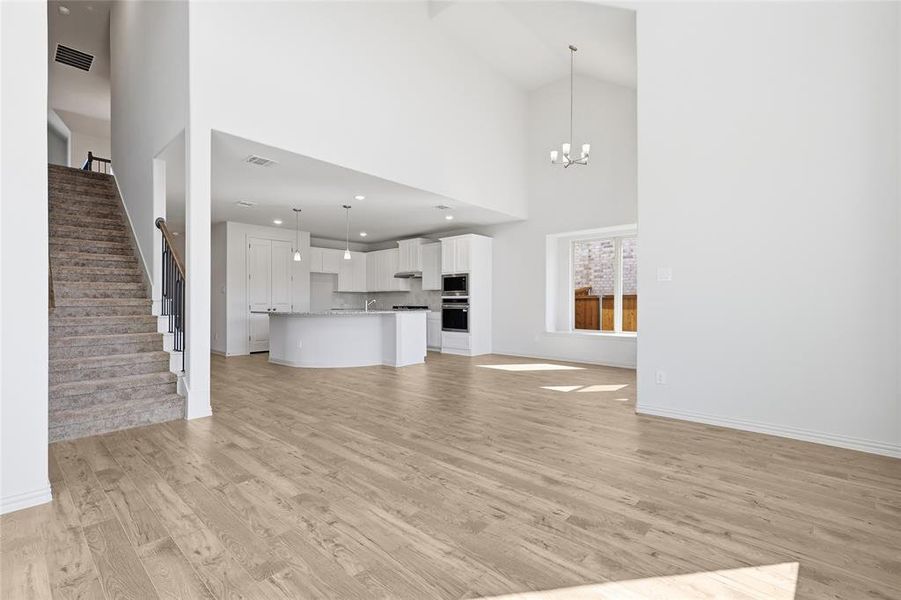 Unfurnished living room with light wood-style floors, stairway, a chandelier, and a towering ceiling