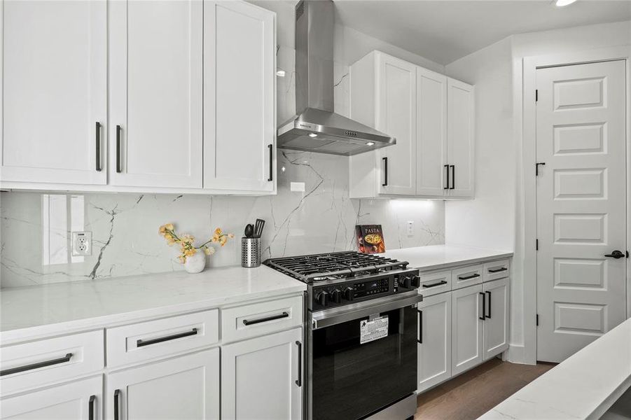 Kitchen with white cabinetry, light stone counters, stainless steel gas stove, and wall chimney range hood