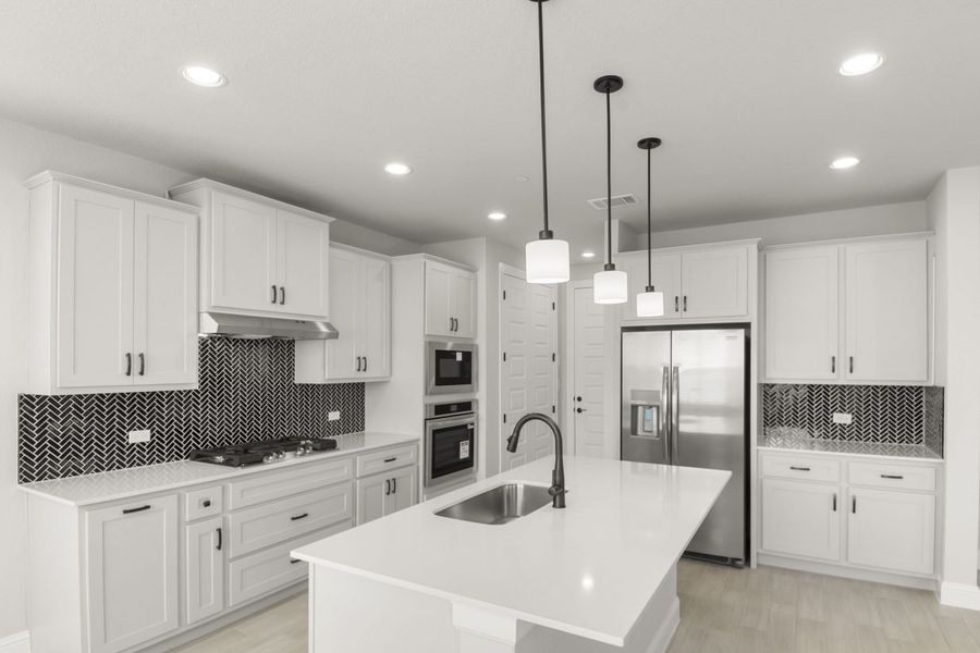 Kitchen interior with grey cabinets and white countertops with black backsplash tile and steel appliances.