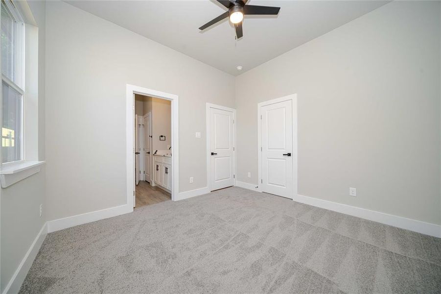 Unfurnished bedroom featuring light colored carpet, ensuite bath, multiple windows, and ceiling fan Unfurnished bedroom featuring light colored carpet, ensuite bath, multiple windows, and ceiling fan