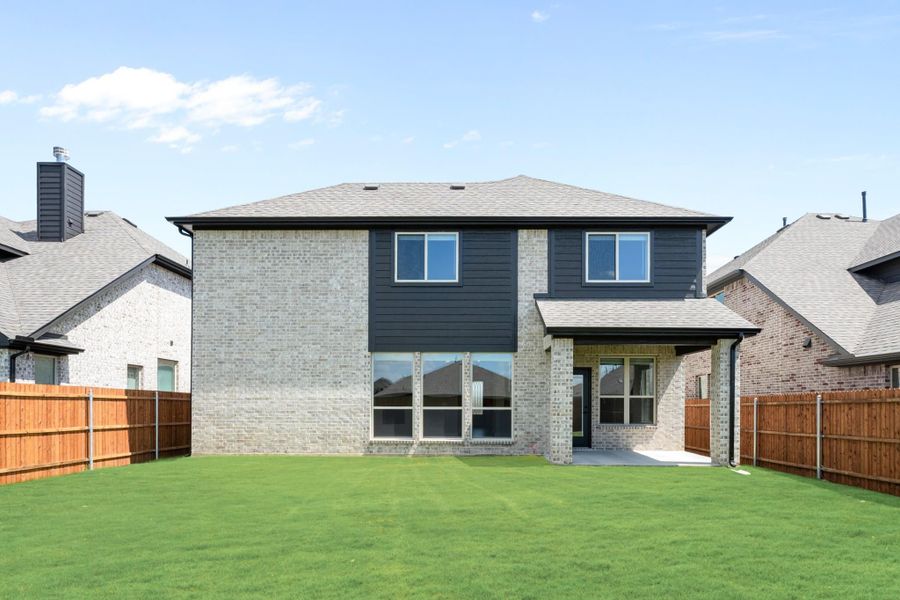 Two-story home rear view with brick and dark siding, large windows, covered patio, and fenced backyard