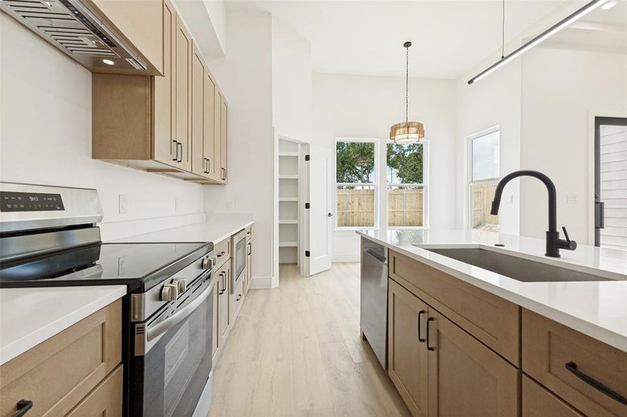 Modern kitchen featuring light wood-finish cabinetry, stainless steel appliances, white countertops, a central island with an undermount sink, and recessed shelving Modern kitchen featuring light wood-finish cabinetry, stainless steel appliances, white countertops, a central island with an undermount sink, and recessed shelving