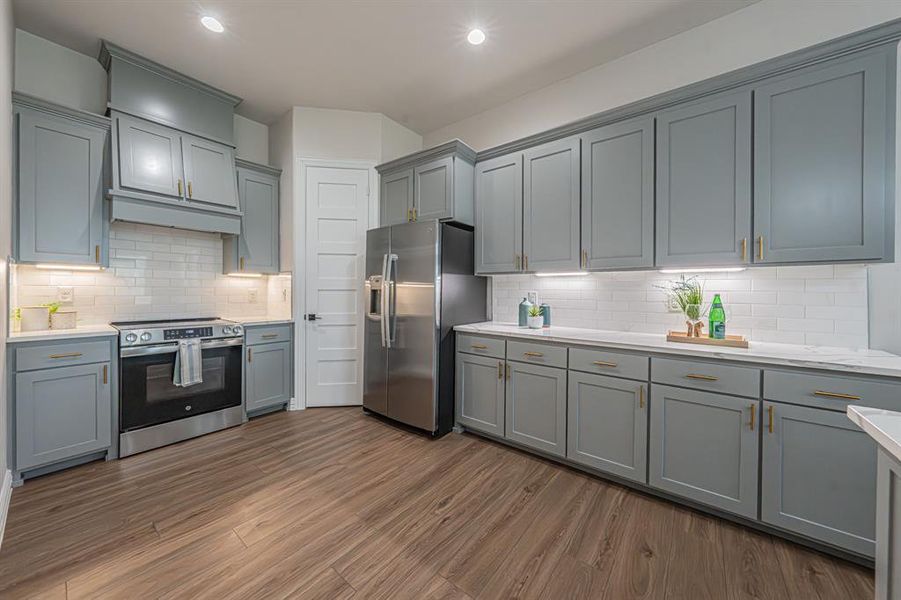 Kitchen with gray cabinetry, stainless steel appliances, dark wood finished floors, decorative backsplash, and light stone countertops Kitchen with gray cabinetry, stainless steel appliances, dark wood finished floors, decorative backsplash, and light stone countertops