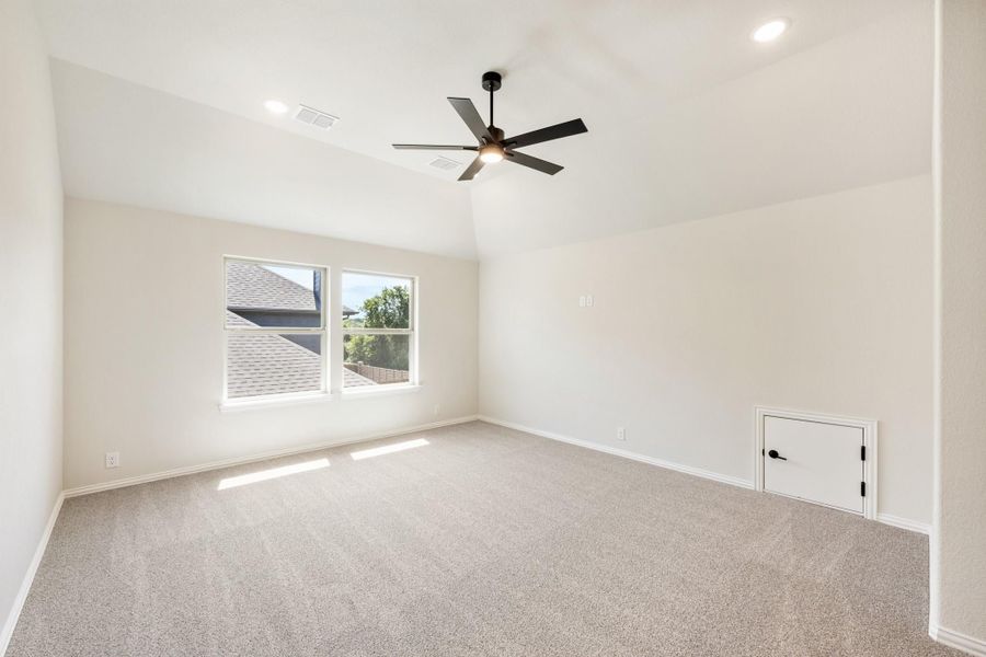 Empty bedroom with vaulted ceiling, black ceiling fan, carpet flooring, and a small access door