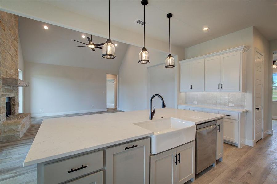 Kitchen featuring light hardwood / wood-style flooring, a center island with sink, dishwasher, a fireplace, and vaulted ceiling with beams