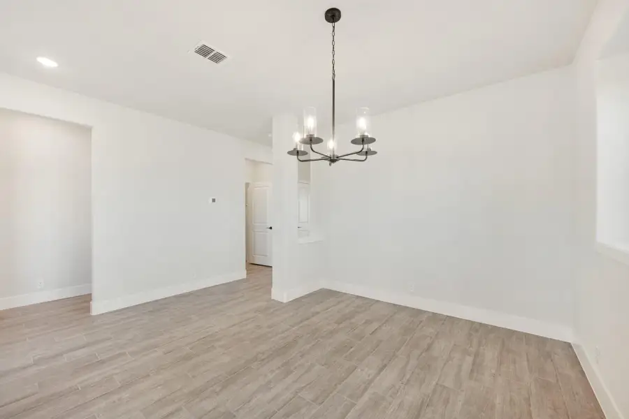Empty dining room with black chandelier, white walls, and light wood-look tile floors
