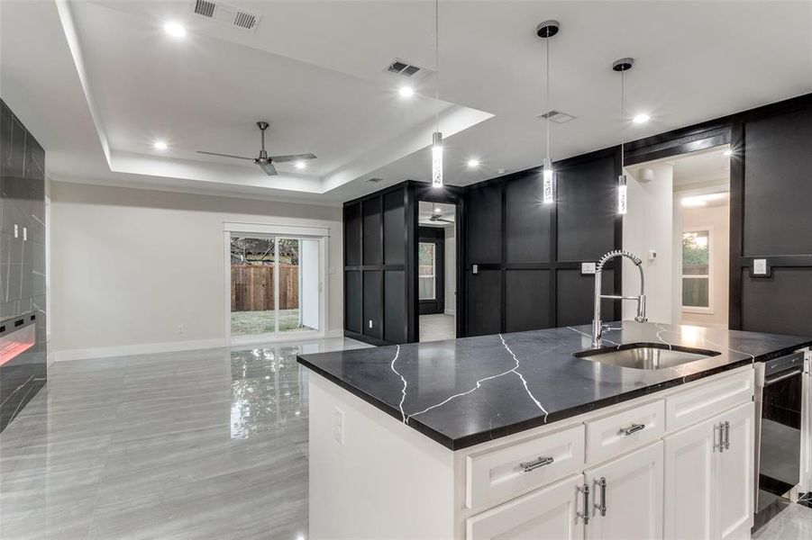 Kitchen with white cabinets, a center island with sink, a tray ceiling, dark stone countertops, and sink