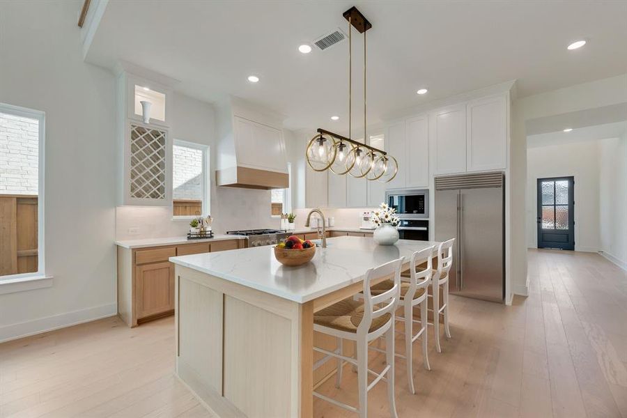 Kitchen with built in appliances, a breakfast bar, light wood-style floors, decorative light fixtures, and recessed lighting Kitchen with built in appliances, a breakfast bar, light wood-style floors, decorative light fixtures, and recessed lighting