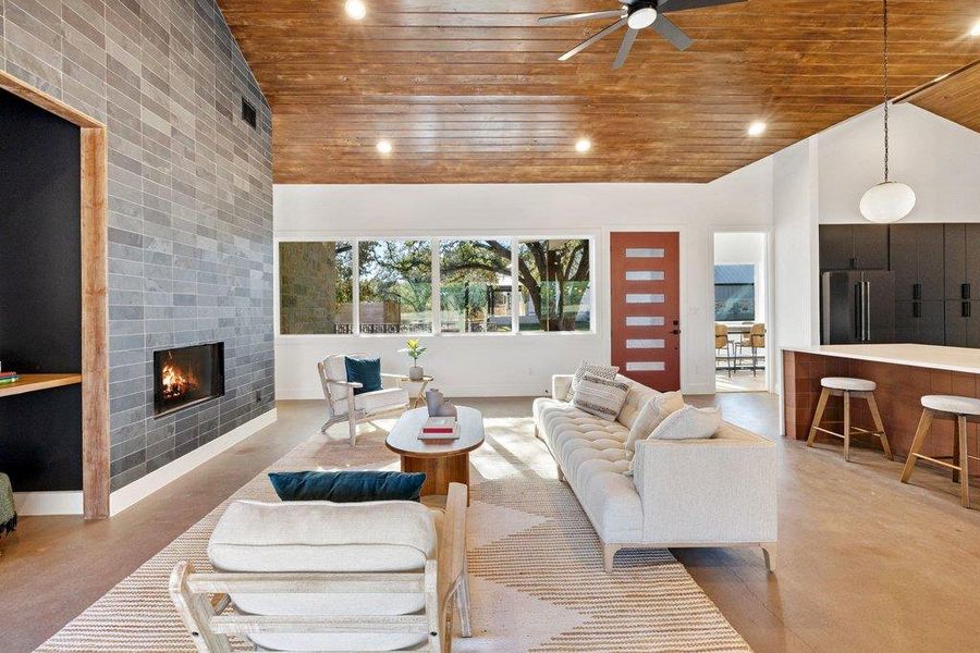 Living room with a tiled fireplace, high vaulted ceiling, wood ceiling, finished concrete floors, and a ceiling fan