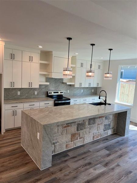 Kitchen featuring stainless steel range with electric cooktop, light stone counters, a large island, backsplash, and white cabinets