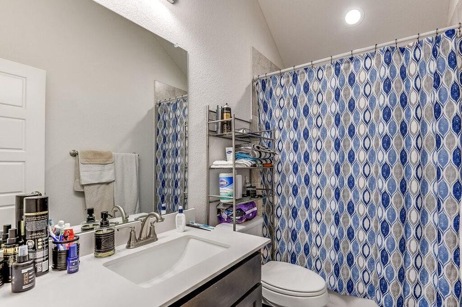 The secondary bathroom features recessed lighting that highlights the tub and shower combo, which is adorned with custom tile.