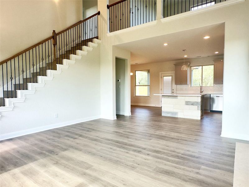 Unfurnished living room with a towering ceiling, plenty of natural light, light wood-type flooring, stairway, and recessed lighting Unfurnished living room with a towering ceiling, plenty of natural light, light wood-type flooring, stairway, and recessed lighting