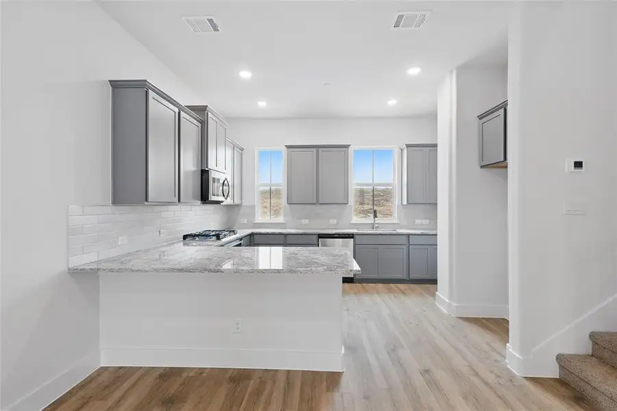 Kitchen featuring tasteful backsplash, a peninsula, gray cabinetry, light stone countertops, and recessed lighting