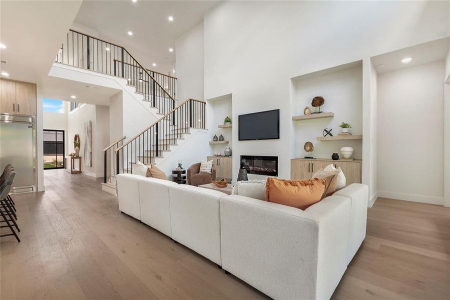 Living room with built in shelves, light wood-type flooring, and a towering ceiling