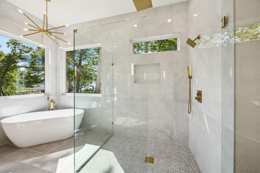 Primary bath with an inviting chandelier, a shower stall, tile patterned flooring, tile walls, and a freestanding bath Primary bath with an inviting chandelier, a shower stall, tile patterned flooring, tile walls, and a freestanding bath