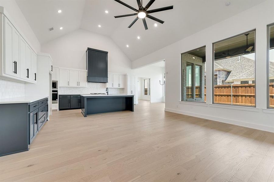 Kitchen featuring open floor plan, white cabinetry, high vaulted ceiling, a center island with sink, and backsplash Kitchen featuring open floor plan, white cabinetry, high vaulted ceiling, a center island with sink, and backsplash