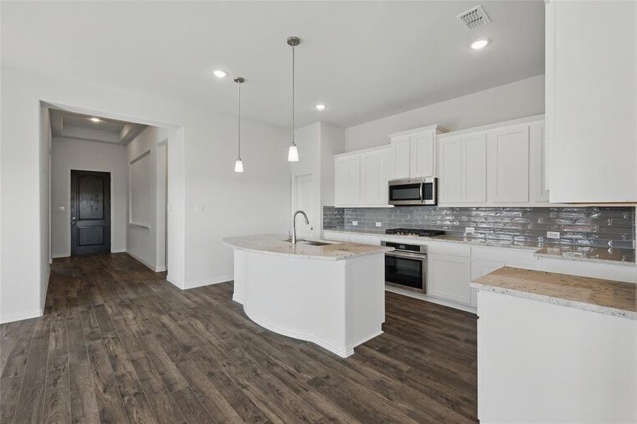 Kitchen with light stone counters, an island with sink, white cabinets, and stainless steel appliances