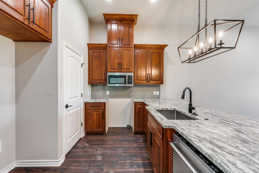 Kitchen with brown cabinetry, decorative backsplash, light stone countertops, dark wood-style flooring, and stainless steel appliances Kitchen with brown cabinetry, decorative backsplash, light stone countertops, dark wood-style flooring, and stainless steel appliances
