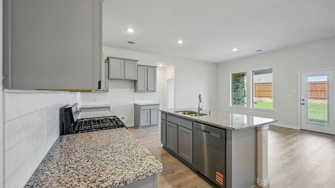 Kitchen featuring gray cabinetry, light stone countertops, stainless steel dishwasher, range with gas cooktop, and decorative backsplash