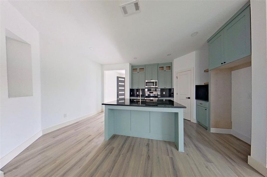 Dual tone kitchen featuring an island with sink, glass insert cabinets, light wood finished floors, stainless steel appliances, and two tone color scheme
