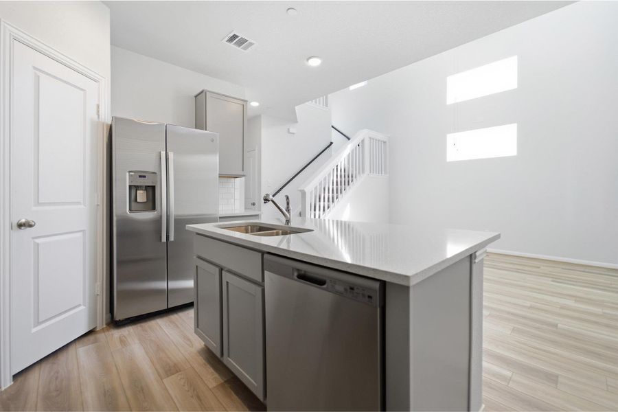 Kitchen featuring gray cabinets, stainless steel appliances, a kitchen island with sink, and light wood-type flooring