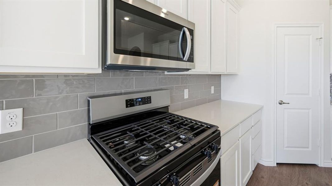 Kitchen with appliances with stainless steel finishes, white cabinets, tasteful backsplash, dark wood-style flooring, and light stone countertops