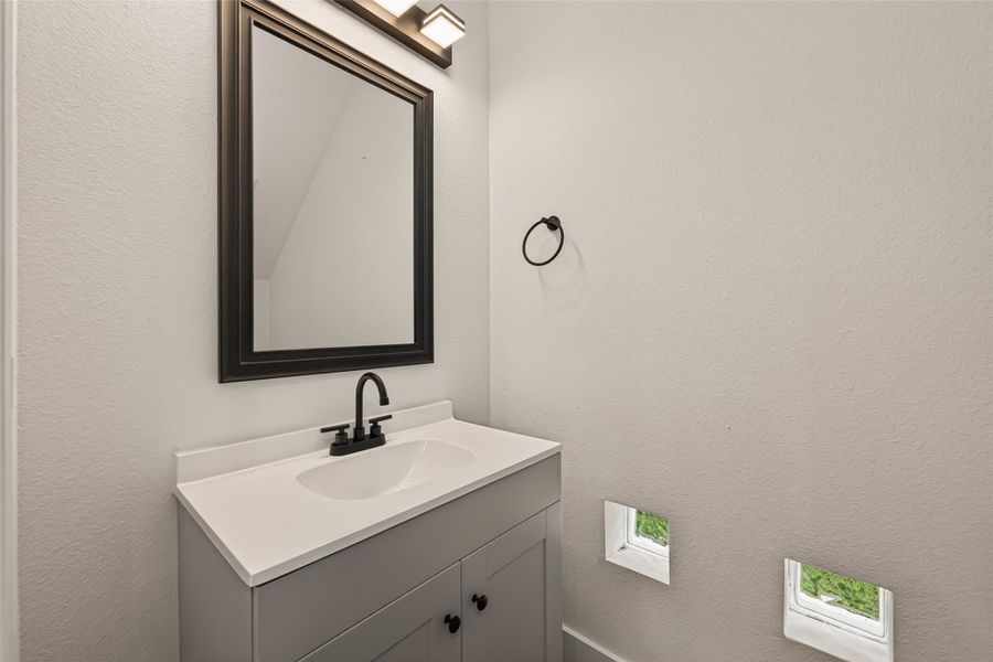 This bathroom features a modern vanity with a sleek black faucet and a large framed mirror. The space is well-lit with contemporary lighting, and small windows provide natural light. Neutral tones create a clean and minimalist look. This bathroom features a modern vanity with a sleek black faucet and a large framed mirror. The space is well-lit with contemporary lighting, and small windows provide natural light. Neutral tones create a clean and minimalist look.