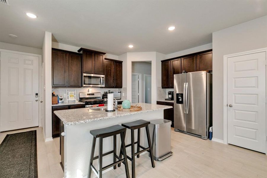 Kitchen with a kitchen bar, stainless steel appliances, light stone counters, dark brown cabinetry, and a kitchen island