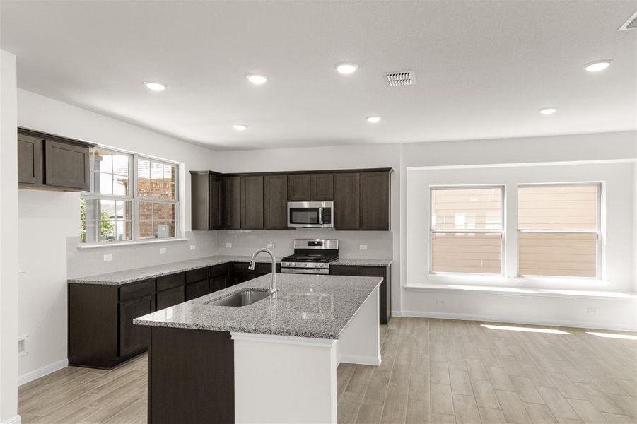 Kitchen featuring light wood-type flooring, stainless steel appliances, a sink, light stone counters, and dark brown cabinets