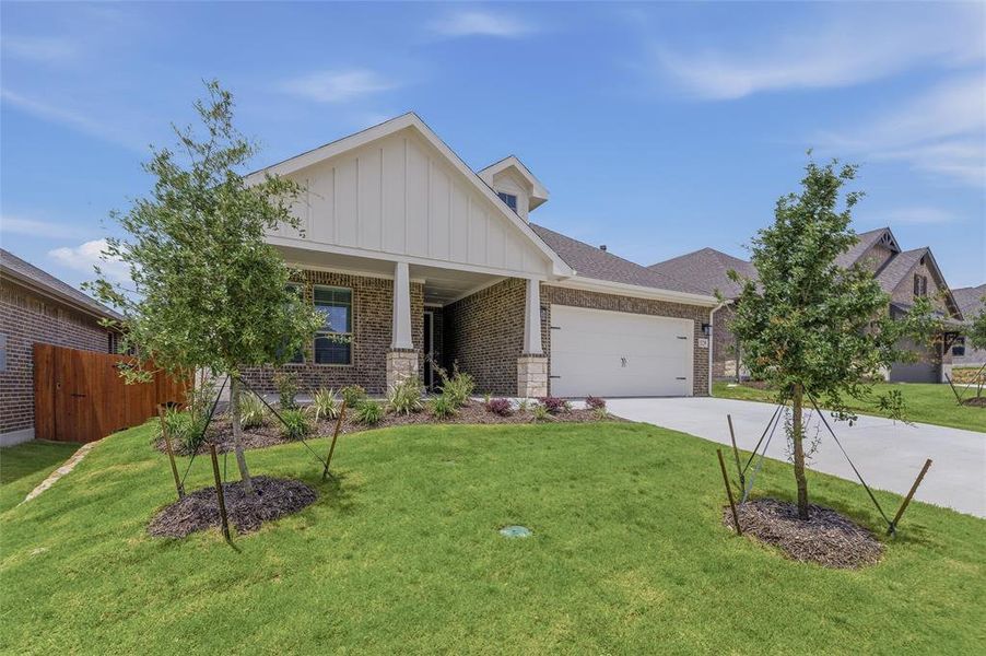 Brick exterior with stone accents, covered entry, attached garage, and a lush lawn with foundational plantings
