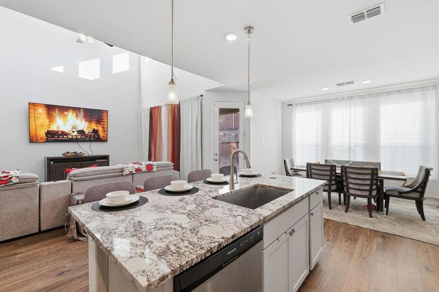Kitchen with pendant lighting, light stone counters, dishwasher, a center island with sink, and open floor plan