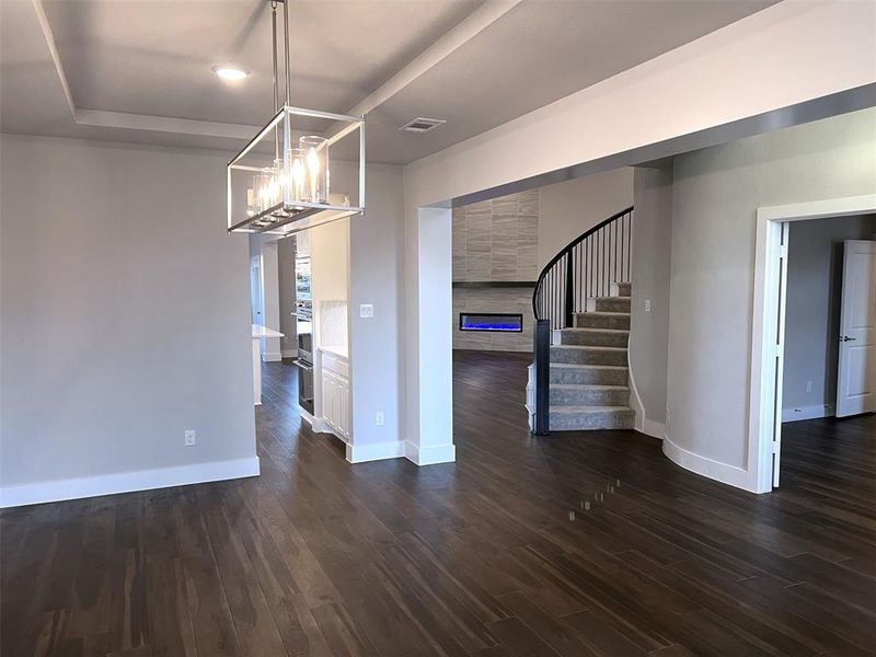 Expansive wood-finish flooring throughout, featuring a tray ceiling with a contemporary chandelier, built-in cabinetry, and a curved staircase with wrought iron balusters Expansive wood-finish flooring throughout, featuring a tray ceiling with a contemporary chandelier, built-in cabinetry, and a curved staircase with wrought iron balusters