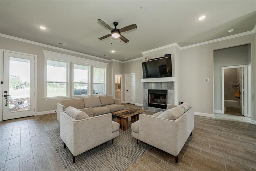 Living room with wood finish floors, crown molding, a ceiling fan, a fireplace, and recessed lighting Living room with wood finish floors, crown molding, a ceiling fan, a fireplace, and recessed lighting