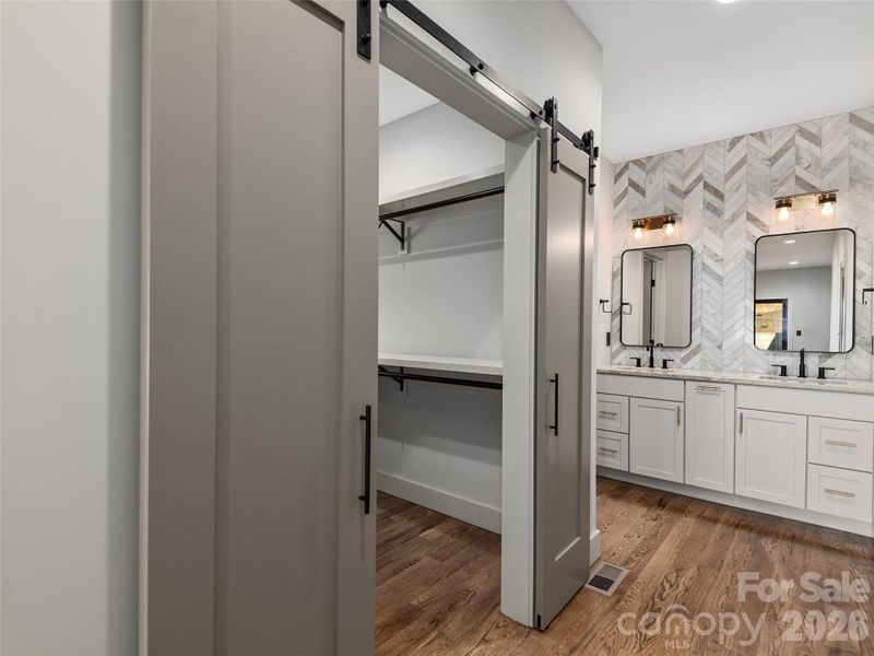 Primary ensuite bath featuring a spacious walk-in closet with wood shelving, sliding barn doors, Wolf cabinetry, granite countertops, and a designer tiled accent wall.
