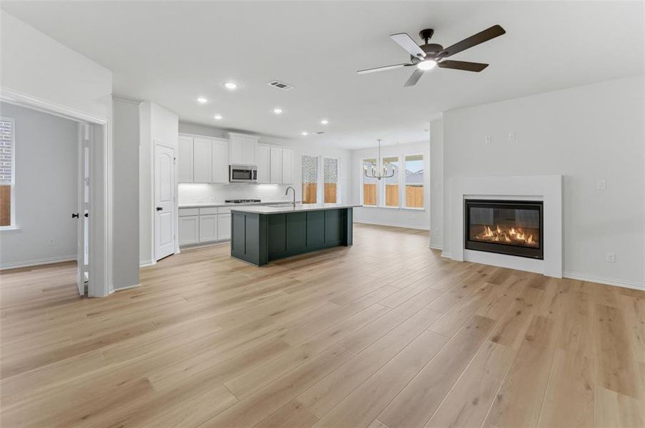 Spacious open-concept area featuring light wood-finish flooring, a contemporary fireplace, and a ceiling fan