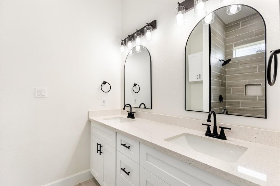 Modern bathroom featuring a dual vanity with sleek black faucets and elegant arch mirrors. The shower area is highlighted with stylish gray tiles, adding a contemporary touch.