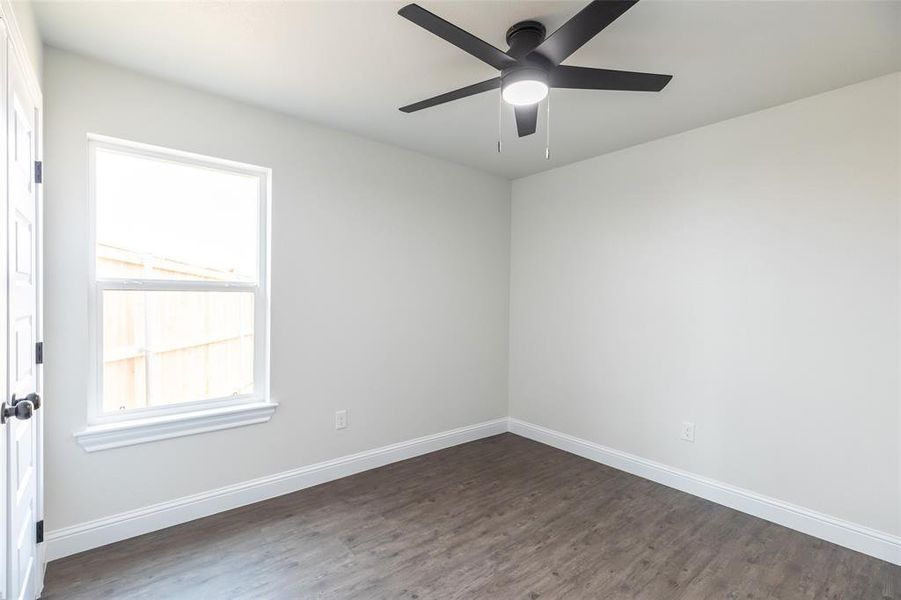 Room featuring wood-finish flooring, a contemporary ceiling fan with integrated lighting, a white framed window, and crisp white baseboards