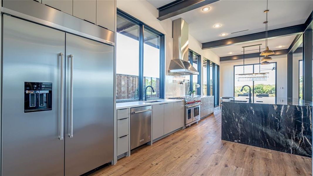 Kitchen featuring sink, wall chimney exhaust hood, decorative light fixtures, high quality appliances, and light wood-type flooring