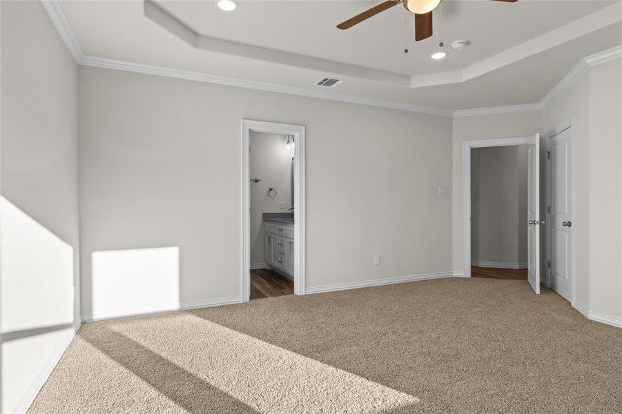 Unfurnished bedroom featuring a raised ceiling, light colored carpet, ensuite bathroom, ornamental molding, and recessed lighting