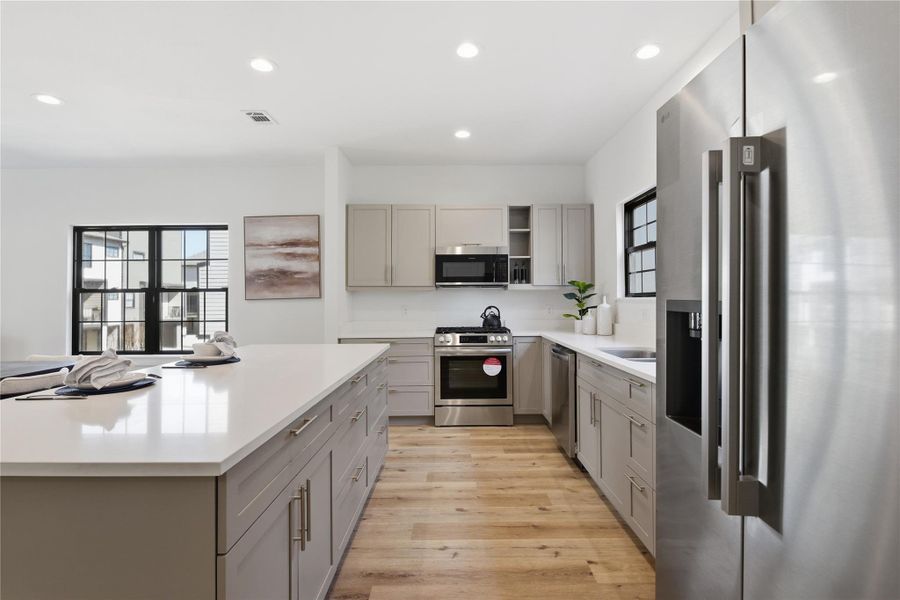 This modern kitchen features sleek cabinetry, a spacious quartz island, warm wood flooring, and abundant natural light from large windows.